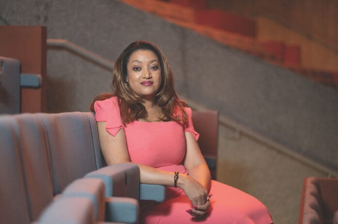 Zimbabwe-born fintech entrepreneur Valerie Moran seated in an auditorium, wearing a coral-pink dress.
